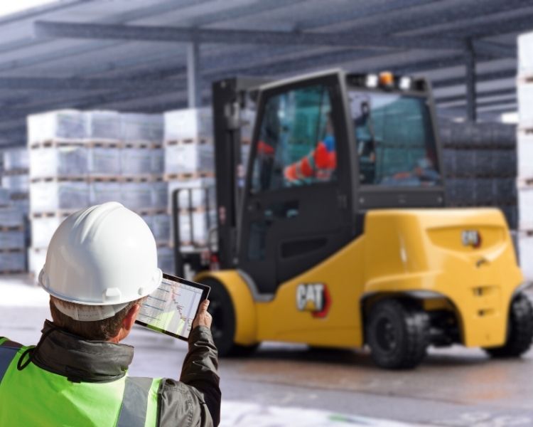 Operations manager viewing forklift telemetry data on a tablet while standing by an electric forklift from Cat lift trucks.