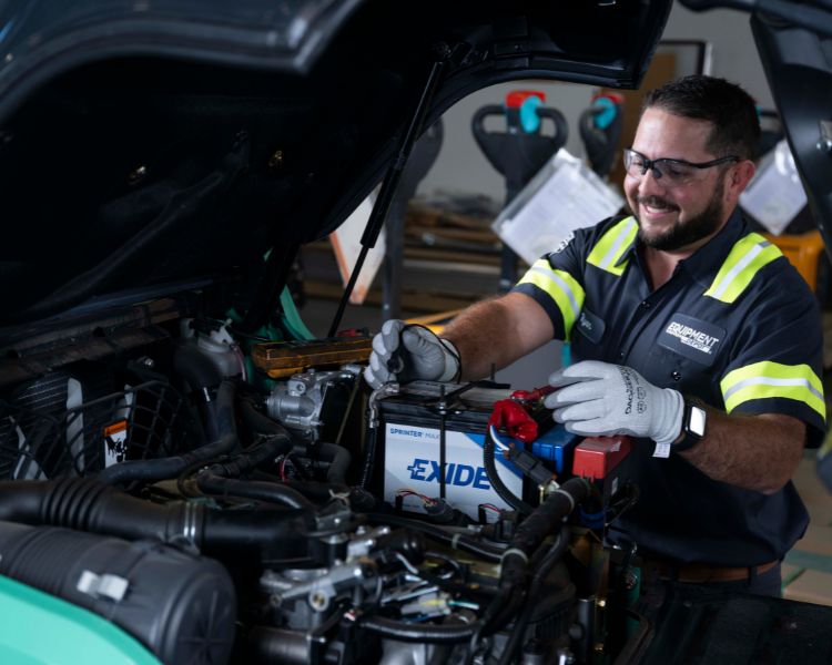 A smiling Equipment Depot service technician working on a forklift and performing a battery inspection.