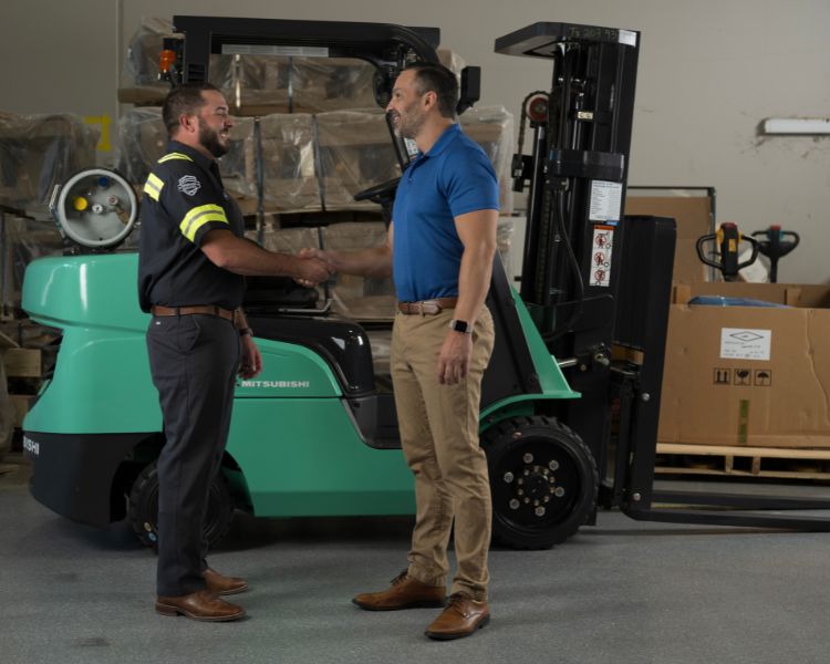 An Equipment Depot service technician shaking hands with a warehouse manager alongside a Mitsubishi forklift truck inside a warehouse.