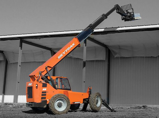 A SkyTrak telehandler extended above the roof of a structure with materials on a pallet on the telehandler's forks.