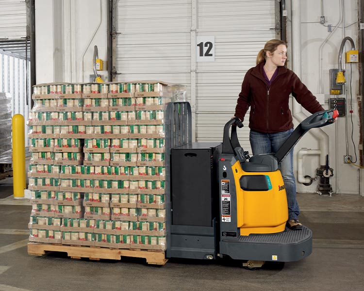 A Class III walkie rider pallet truck with an operator on the platform and beverage pallets on the forks.